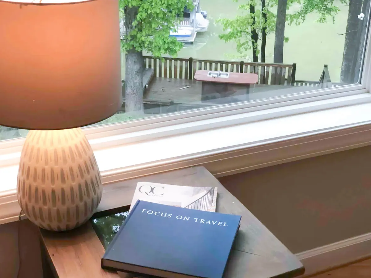 A cozy reading nook featuring a comfortable chair beside a lamp, with books arranged nearby and a window offering an inviting view outside. The scene conveys a sense of relaxation and gentle anticipation, as if planning the next adventure or reflecting after a day outdoors.