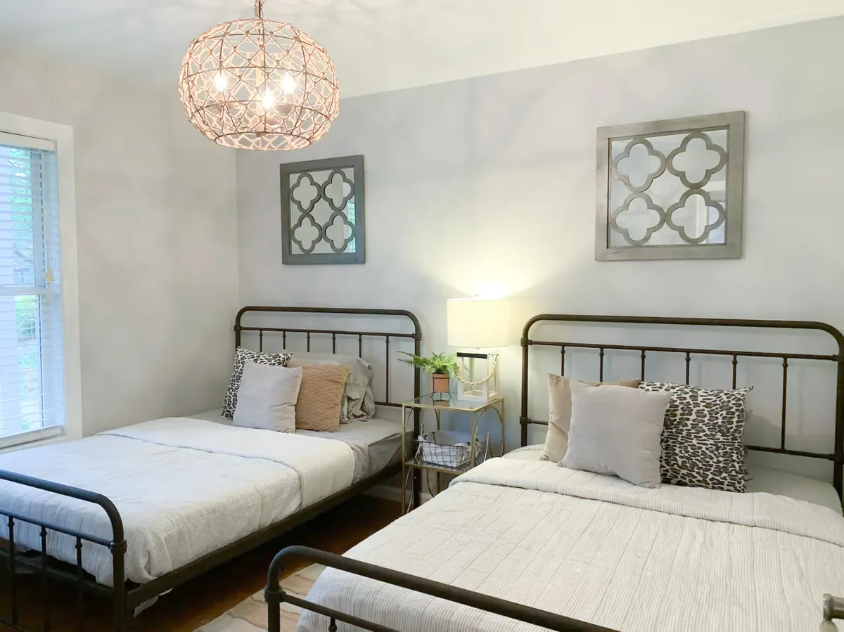 A comfortable private bedroom with two metal bed frames, decorative pillows, a chandelier, and wall art. The ambiance is cozy and inviting, providing a quiet, restful retreat adjacent to the entertainment areas.