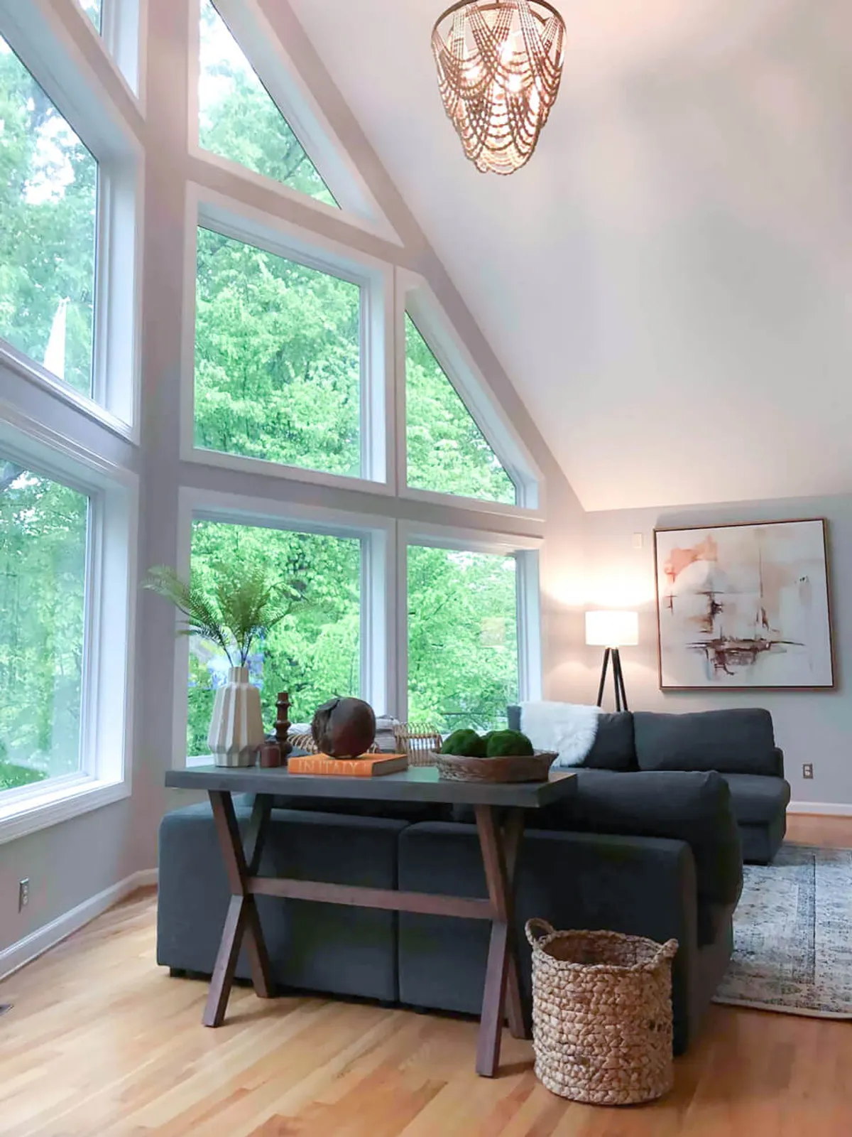 A spacious living area featuring a comfortable sofa, coffee table, and large windows that flood the room with natural light. The windows provide expansive views of the outdoors, and the room is decorated with tasteful artwork and a standing lamp, creating a cozy environment perfect for relaxing or socializing.