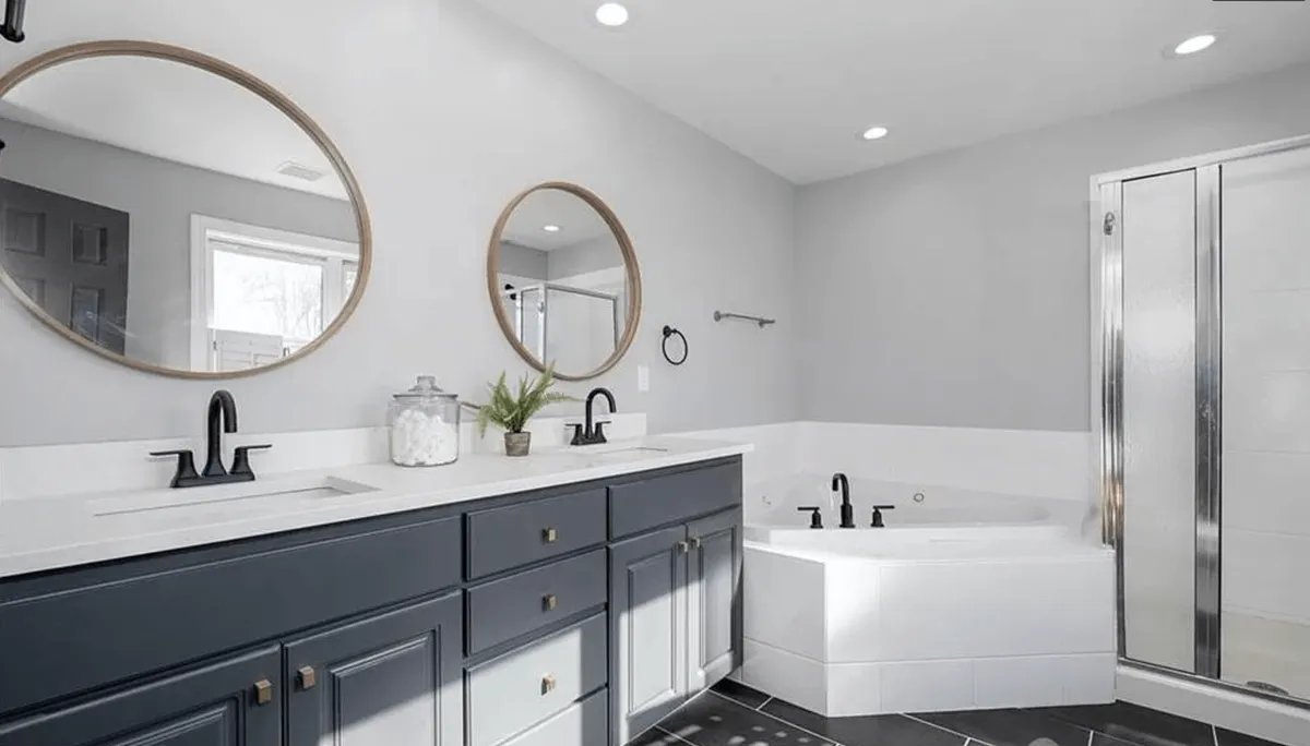 This bathroom scene presents a modern double-sink vanity flanked by mirrors and a luxurious freestanding soaking tub. The clean lines, ample lighting, and spa-like ambiance underscore a sense of indulgence and relaxation.