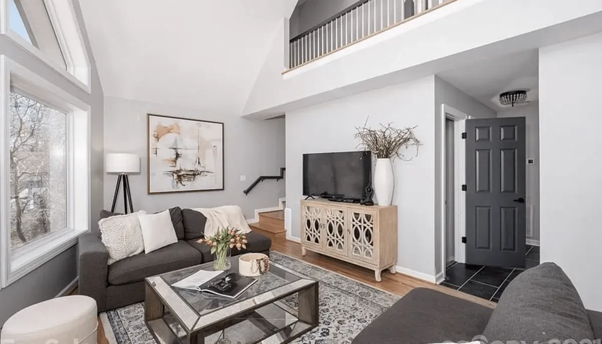A spacious and sunlit living room with a large window letting in natural light, comfortable seating, a decorative coffee table, and an art piece on the wall. The scene radiates warmth and comfort, suggesting a welcoming environment for both families and their pets.