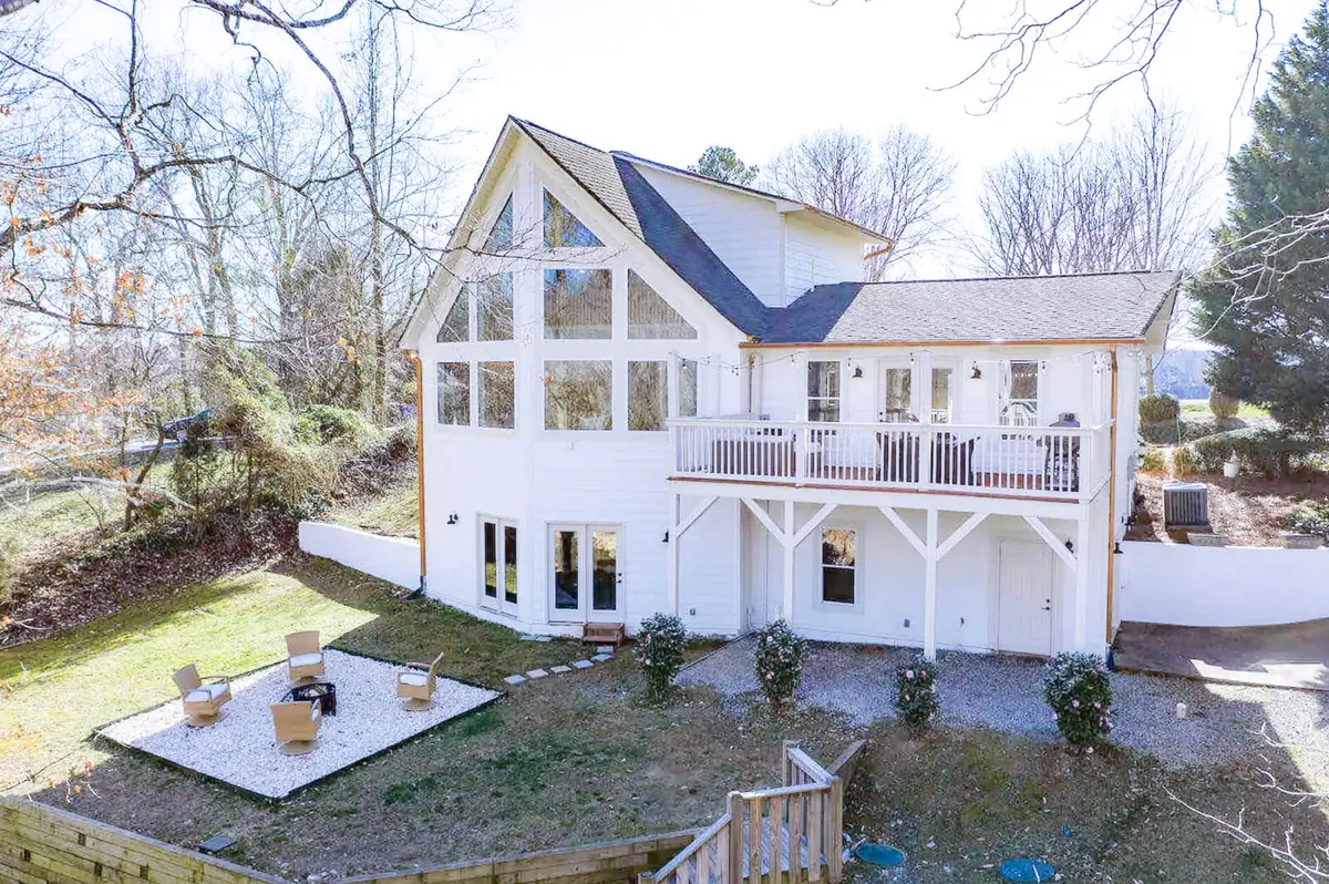 A wide exterior view showcasing the home’s large deck area with comfortable seating, a crackling wood-burning fire pit, and a beautifully landscaped garden. The image captures people gathered around the fire pit, enjoying the tranquil sunset and making memories outdoors.