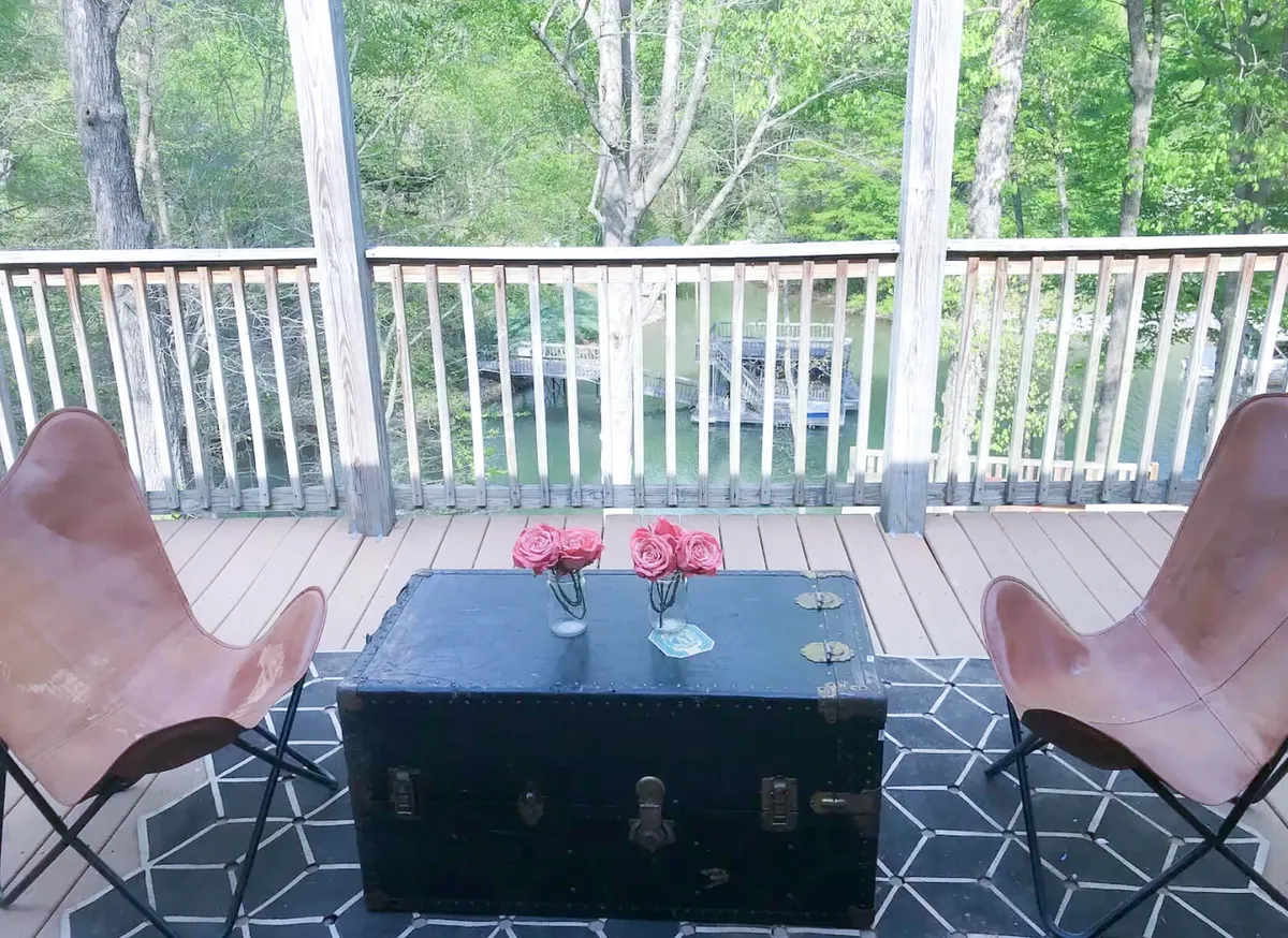 The image captures a serene outdoor seating area, with two butterfly chairs, a black trunk used as a table, a vase of roses, and a lush view of surrounding greenery. The space is bathed in natural light, perfect for relaxing, socializing, or enjoying the outdoors together.