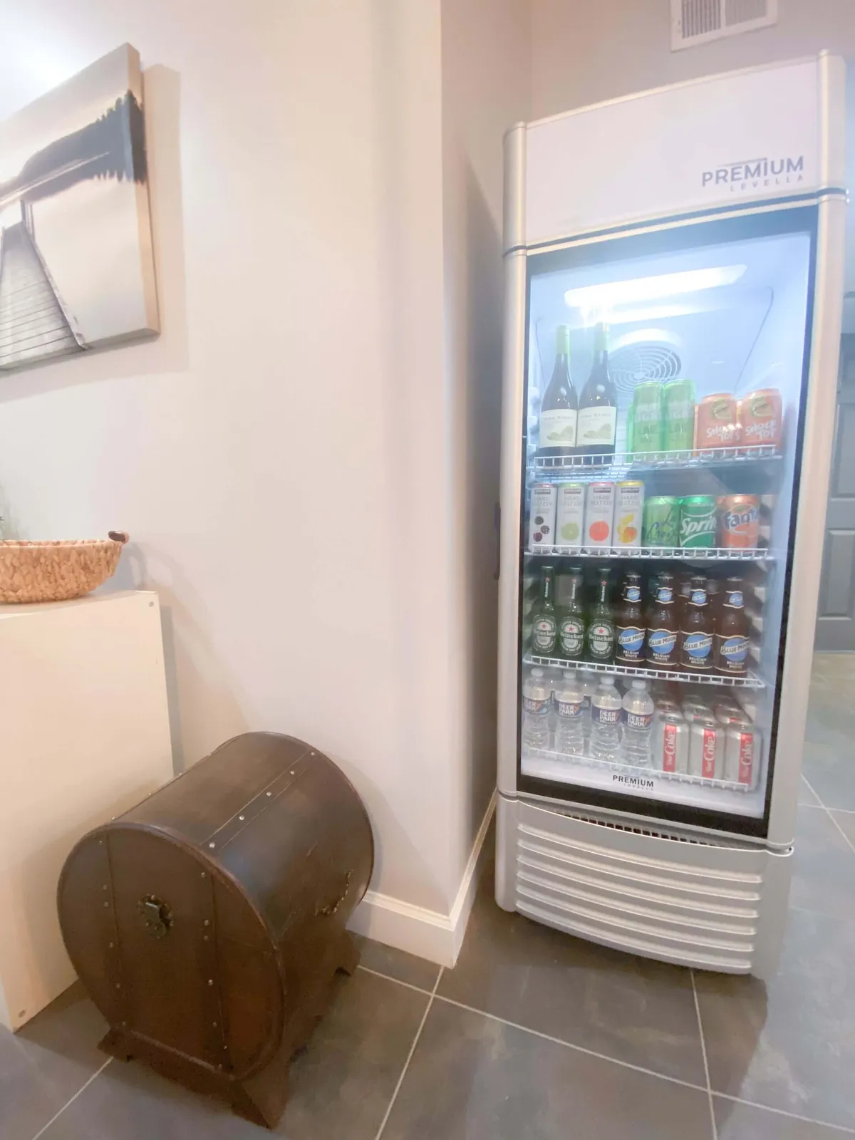 A relaxed bar area featuring a refrigerator, wooden chest, and wall art, with people gathering for drinks and casual conversation. The ambiance is welcoming and encourages entertaining and socializing, ideal for hosting friends and sharing laughs.