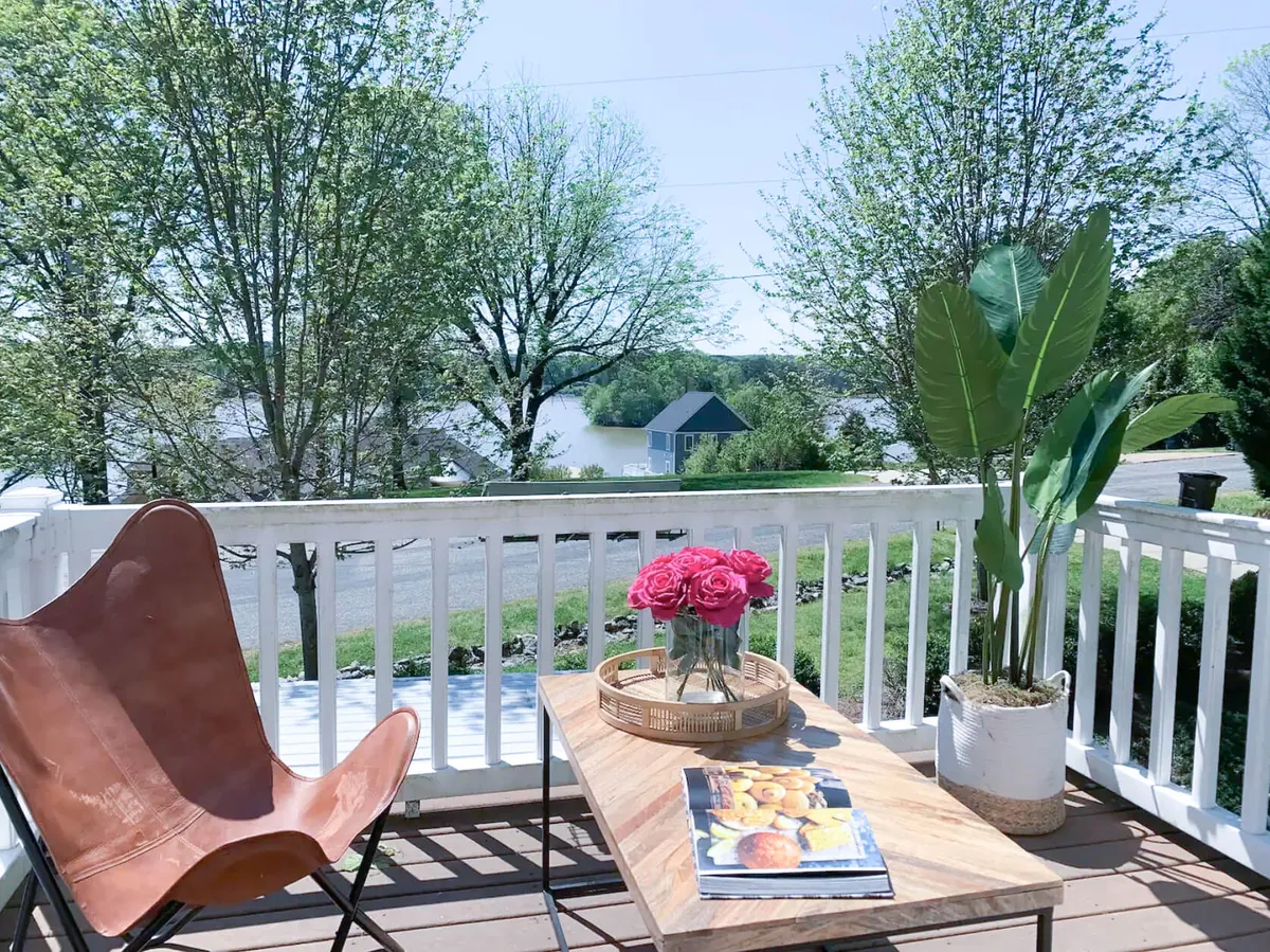 An exterior seating area featuring a comfortable leather chair and coffee table, set against a stunning lake view with potted plants adding a touch of homey comfort. The scene evokes relaxation and outdoor leisure with the water as a backdrop.